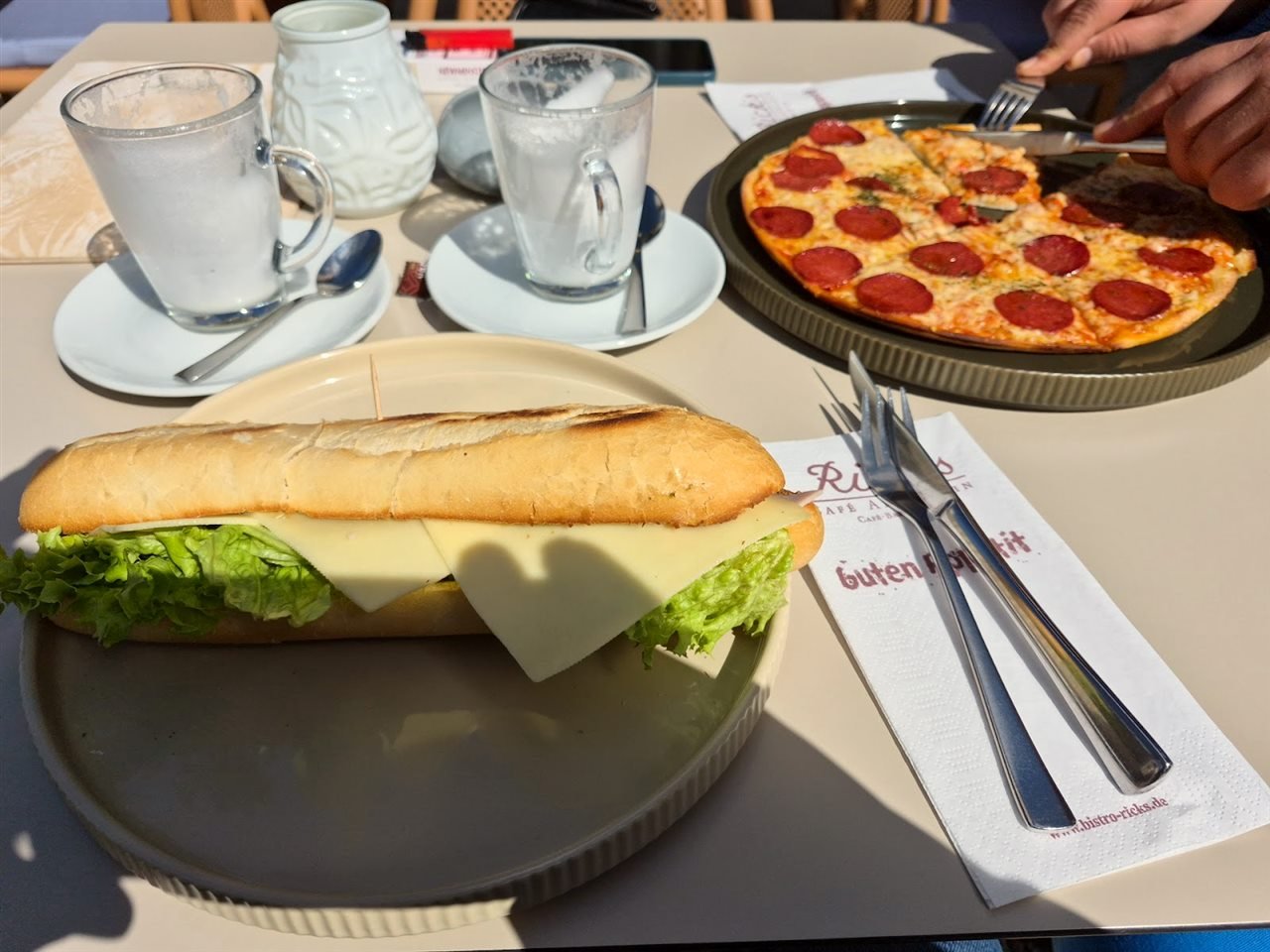 Gedeckter Tisch bei Rick's mit Pizza, Baguette und Cappuccino